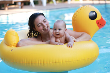 happy mother with a toddler baby boy playing in an inflatable duck ring in a swimming pool
