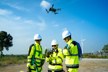 Fototapeta premium An engineer in a hard hat and safety vest operates a drone to inspect towering wind turbines in a remote area.