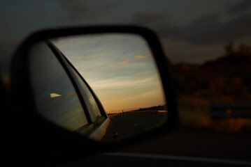 Rear view mirror of a traveling vehicle, in the reflection you can see the road at sunset. Concept: returning home after a car trip.
