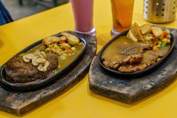 Two sizzling hot plates, one with a hearty beef bulgogi potato and the other with a flavorful chicken papers, served with a variety of sides. 