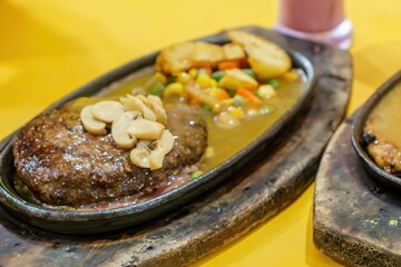 A close-up of a thick, juicy beef steak and fluffy roasted potatoes on a hot plate. The contrast between the red meat, golden potatoes, and green herbs creates a visually appealing dish.