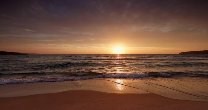 Sunset over ocean beach shore with splashing waves on the sand. Sea sunrise video