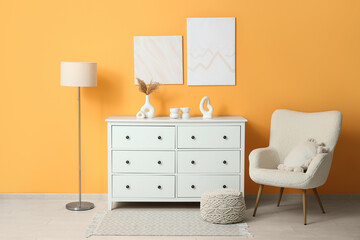 Comfortable armchair, pictures and white chest of drawers in interior of living room