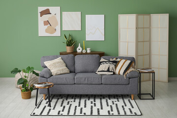 Comfortable sofa, coffee table, pictures and folding screen in interior of living room