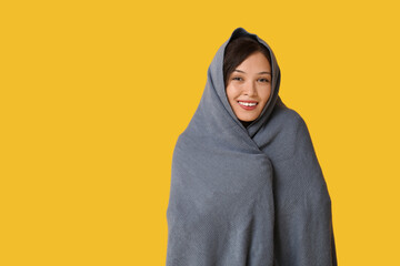 Beautiful young happy Asian woman with warm soft plaid on yellow background