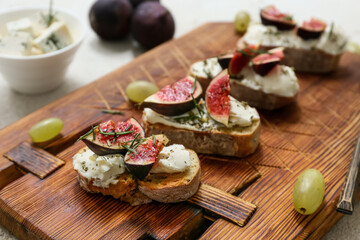 Wooden board of delicious fig bruschetta with ricotta cheese and grapes on white background