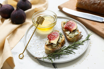 Plate of delicious fig bruschetta with blue cheese and bowl of honey on white background, closeup