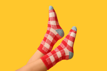 Legs of young woman in warm checkered socks on yellow background