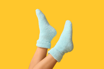 Legs of young woman in warm blue socks on yellow background