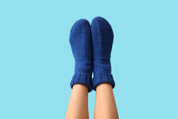 Legs of young woman in blue knitted socks on color background