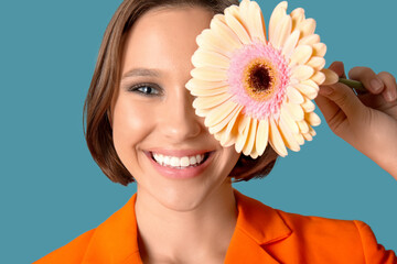 Beautiful young woman with stylish makeup holding gerbera flower on blue background, closeup