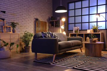 Interior of living room with soft sofa, coffee table and glowing lamps at evening
