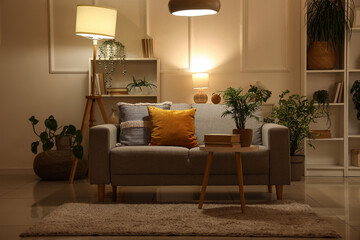 Soft sofa, coffee table and glowing lamp in interior of living room at evening