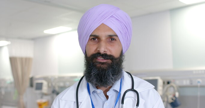 Portrait of happy biracial sikh male doctor in turban looking at camera at hospital, in slow motion