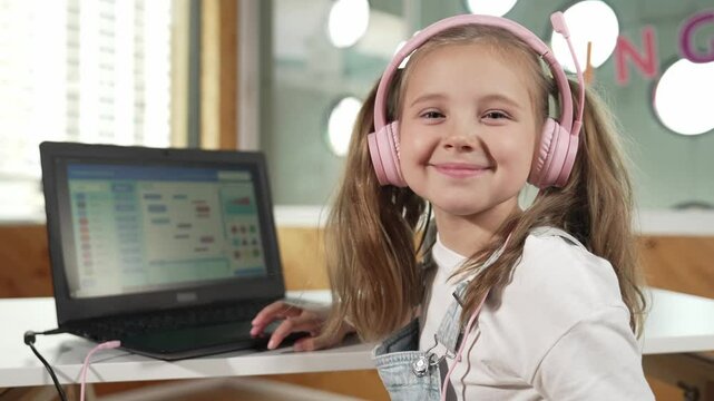 Smiling girl show system programing or coding program in STEM technology education. Child wearing headphone while working by using laptop writing code and turn around to look at camera. Erudition.