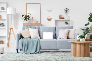 Interior of light living room with laptop on sofa and plants