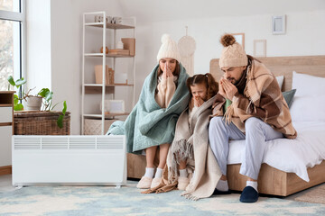 Frozen family sitting near electric convector heater in bedroom