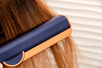 Fototapeta premium Close-up shot of a hair straightener gliding through long, light brown hair. Beauty fashion and styling tools