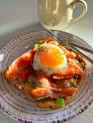 Toast with salmon, poached egg and avocado on white plate. Morning sun light. Vertical