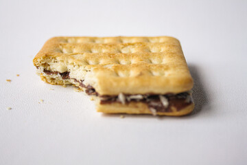 Bitten sandwich biscuit with chocolate filling on white background