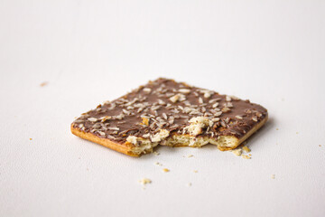 Bitten chocolate biscuit with coconut sprinkles on white background