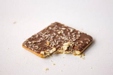 Bitten chocolate biscuit with coconut sprinkles on white background