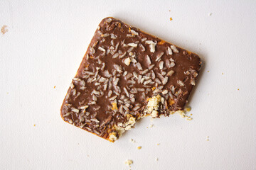 Bitten chocolate biscuit with coconut sprinkles on white background