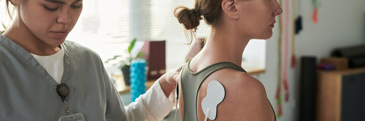 Medical professional placing electrode pad on patient's upper back in clinic environment. Patient with shoulder exposed, receiving treatment from healthcare worker © pressmaster