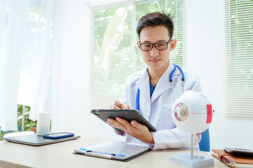 A male doctor wearing glasses sits at a desk in a hospital, explaining eye diseases like glaucoma,...