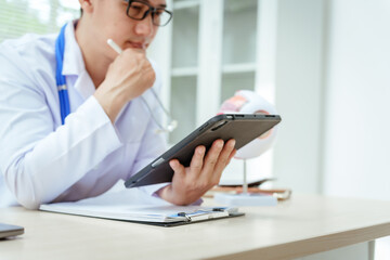 A male doctor wearing glasses sits at a desk in a hospital, explaining eye diseases like glaucoma,...