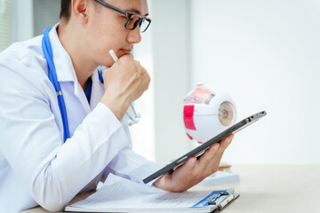 A male doctor wearing glasses sits at a desk in a hospital, explaining eye diseases like glaucoma,...