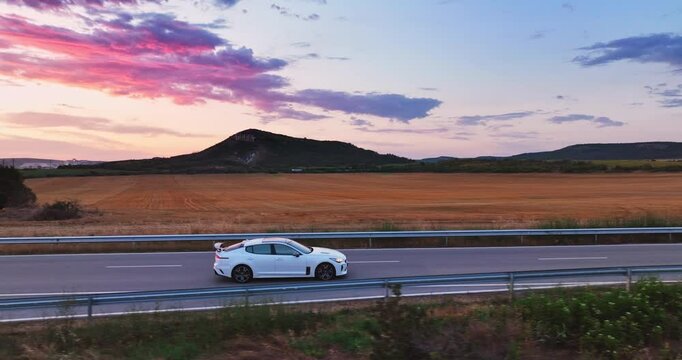 Car Driving on Countryside Road Surrounded by agricultural fields during scenic sunset