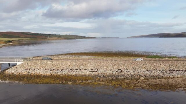 Tracking shot of electric car driving on Kyle of tongue causeway in Scotland