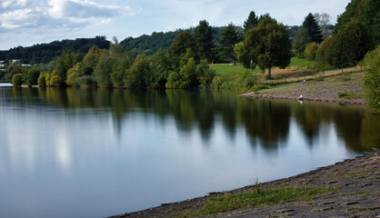 Shore on the edge of a lake surrounded by green trees in the background on a summer afternoon  in Germany.