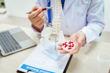 A male doctor wearing glasses sits at a desk, explaining a spine model, discussing spinal anatomy,...