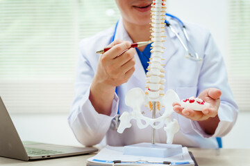 A male doctor wearing glasses sits at a desk, explaining a spine model, discussing spinal anatomy,...