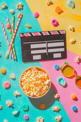 Movie night essentials colourful flat lay: clapperboard, popcorn, straws, 3D glasses, vibrant background