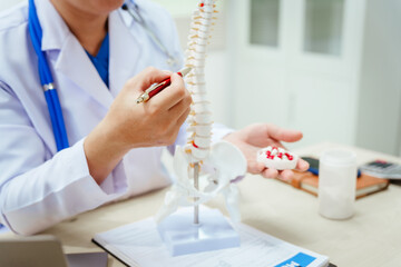 A male doctor wearing glasses sits at a desk, explaining a spine model, discussing spinal anatomy,...