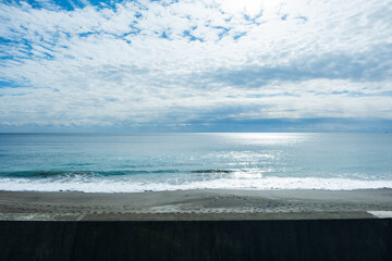 太陽の光日差しに照らされ反射した日光がキラキラ輝く海の風景　遠くの太平洋の水平線　穏やかな波と青空・砂浜と雲の海景　バカンス・リゾート・チル・観光・旅行の美しい景色