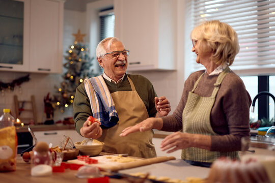 Cheerful senior couple having fun while making Christmas cookies in the kitchen.