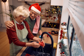 Happy senior couple doing the dishes after making cookies for Christmas in the kitchen.