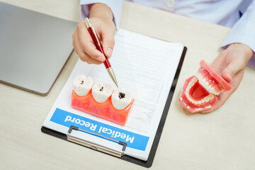 A bespectacled male doctor sits at a desk explaining about tooth decay, its causes such as plaque...