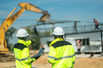 Two engineers in high-visibility jackets and helmets reviewing plans on a laptop at a construction site with an excavator in the background, representing safety, precision, and technological planning.