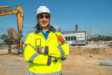An engineer in visibility jacket and helmet standing confidently at a construction site with...