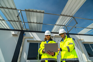 Two engineers in high visibility jackets discussing plans on a laptop at a modular construction site. A window reflection shows their teamwork and professionalism in site planning and management.