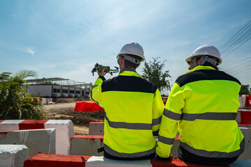 Two engineers wearing high visibility jackets discuss construction progress near concrete...
