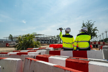 Two engineers wearing high visibility jackets discuss construction progress near concrete...