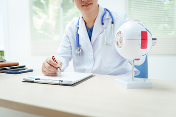 A male doctor wearing glasses sits at a desk in a hospital, explaining eye diseases like glaucoma,...