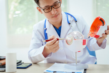 A male doctor wearing glasses sits at a desk in a hospital, explaining eye diseases like glaucoma,...