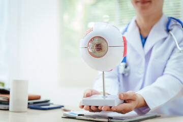 A male doctor wearing glasses sits at a desk in a hospital, explaining eye diseases like glaucoma,...